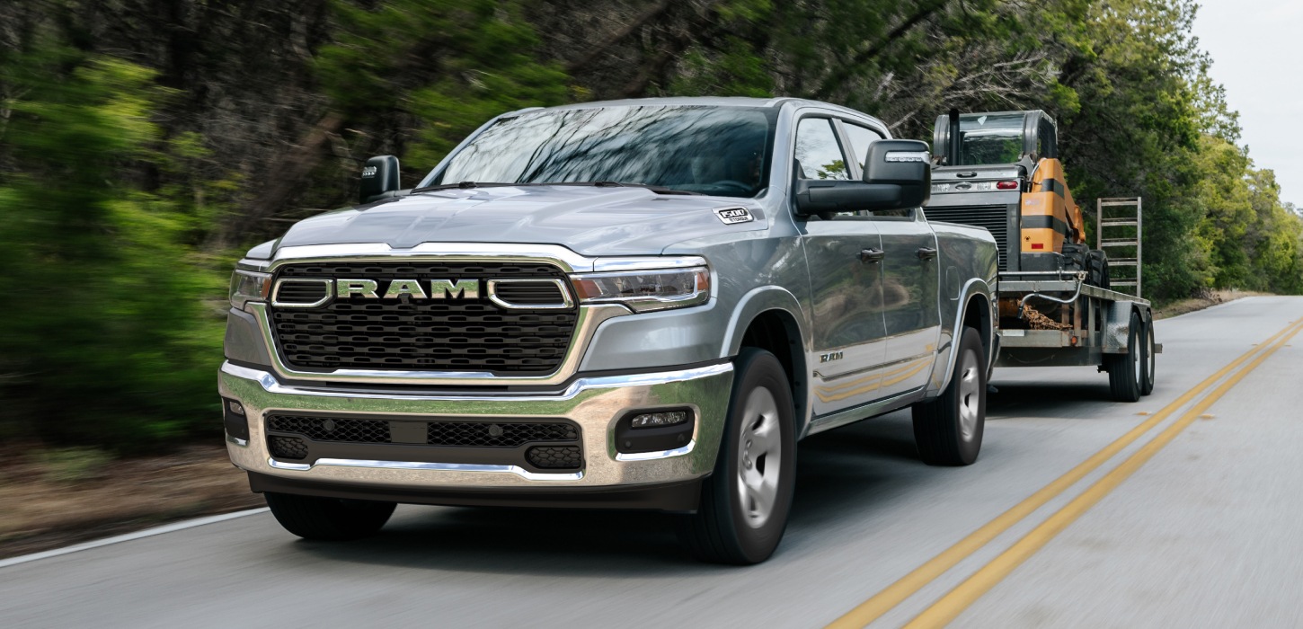 Una Ram 1500 Big Horn 4x4 Crew Cab 2026 plateada remolcando equipos motorizados mientras viaja por una carretera.