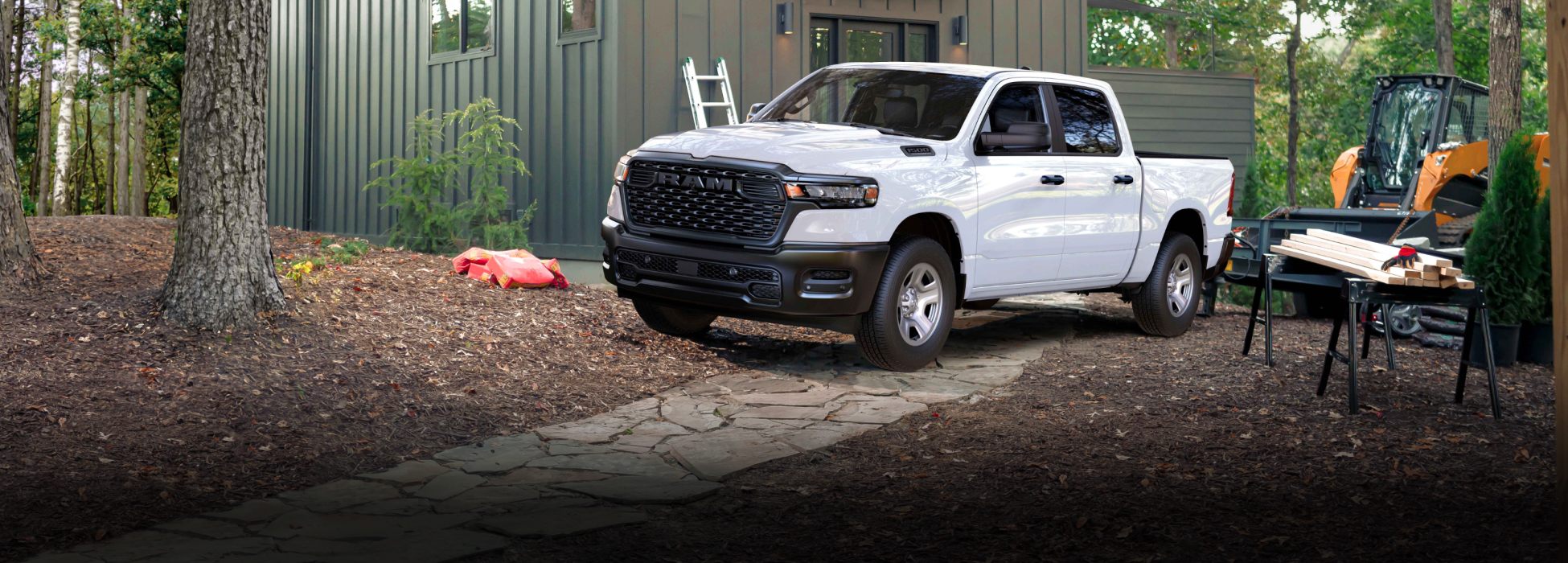 Una Ram 1500 Tradesman 4 x 4 2026 blanca estacionada al lado de una cabaña en el bosque.