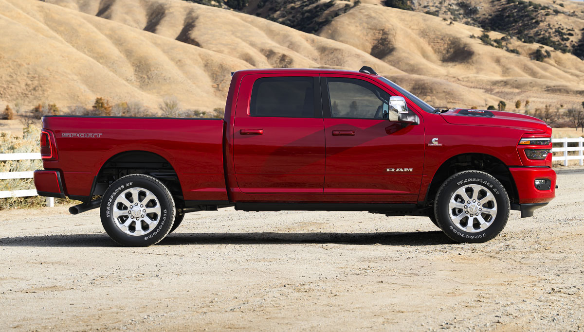 Se muestra un perfil del lado del pasajero de una Ram 2500 Laramie 2026 roja en un rancho en el desierto.