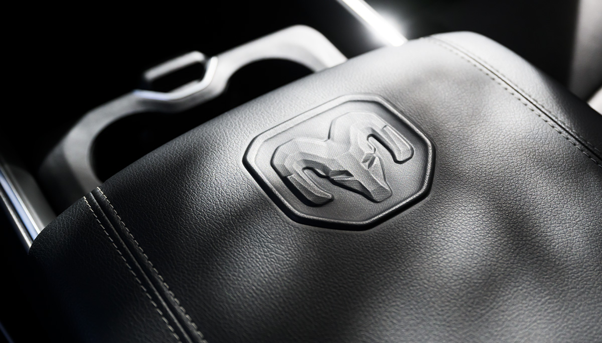 Se muestra el apoyabrazos acolchado en la consola central con la cabeza de carnero de Ram en la Ram 2500 2026.