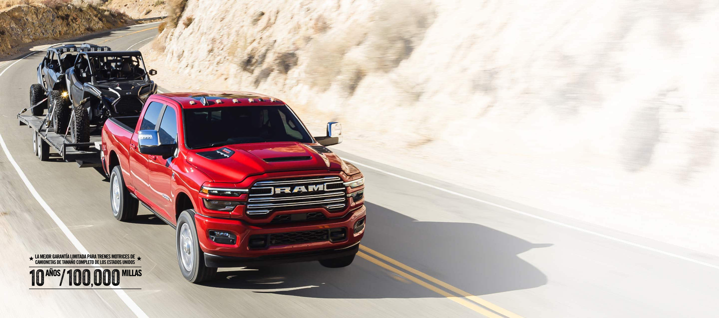 Una Ram 2500 Laramie 4x4 Crew Cab 2026 roja circulando por una carretera en las montañas, mientras remolca dos ATV. Garantía limitada de 10 años/100,000 millas.