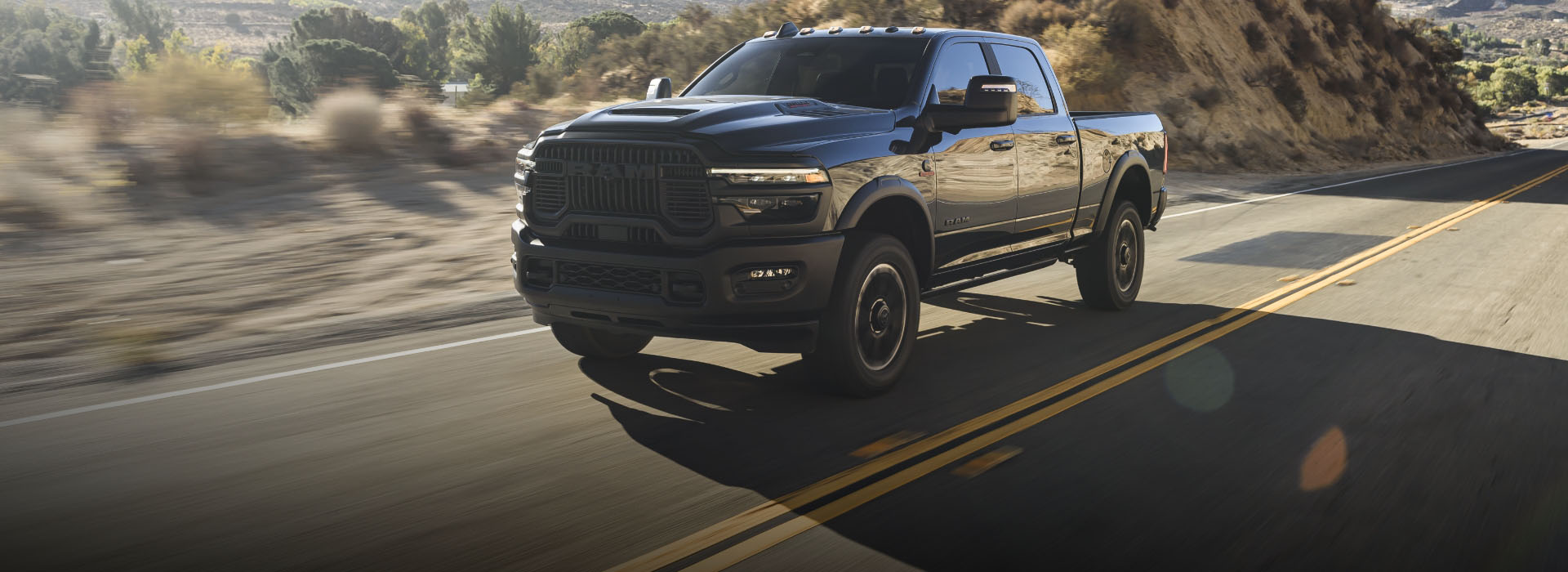 A black 2026 Ram 2500 Rebel traveling on a highway in the desert. El fondo está borroso para indicar que la camioneta está en movimiento.
