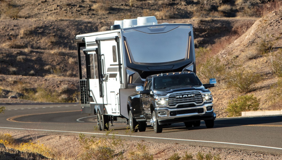Se muestra una Ram 3500 2026 negra circulando por una carretera de montaña, remolcando un RV.