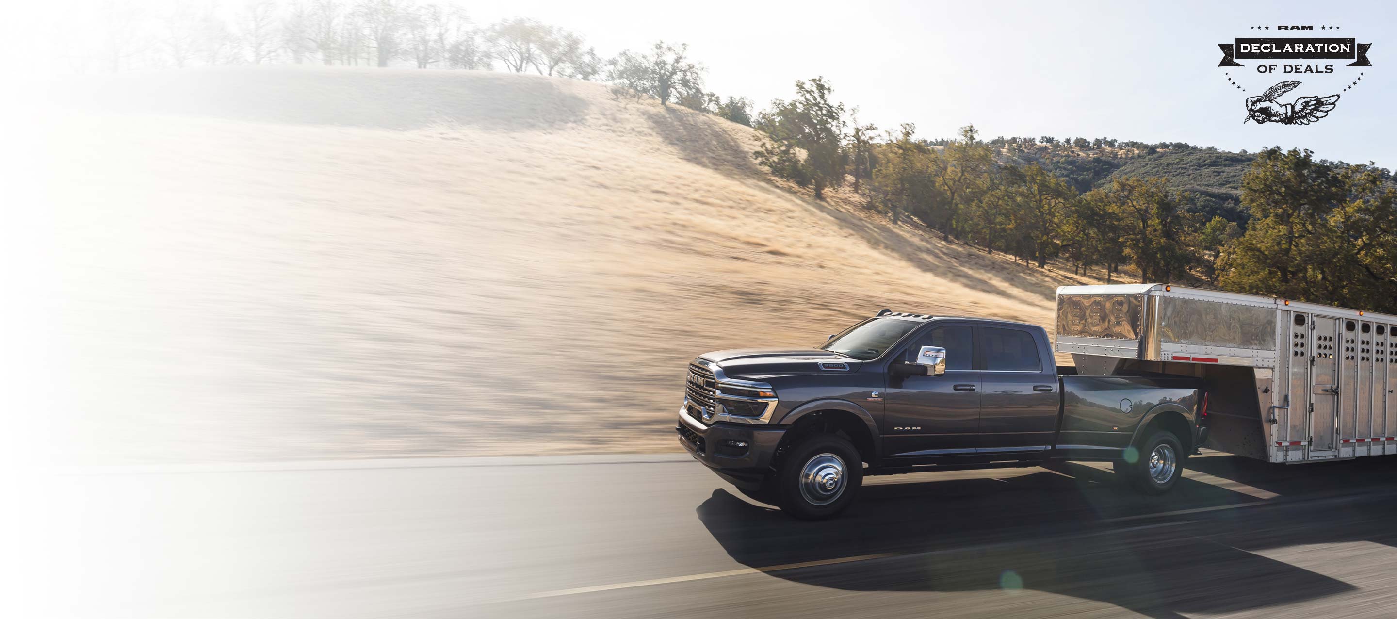 Una Ram 3500 Limited Longhorn 4x4 Crew Cab 2026 gris acarreando un remolque de quinta rueda grande para ganado mientras circula por una carretera. Evento de ventas Declaración de ofertas.