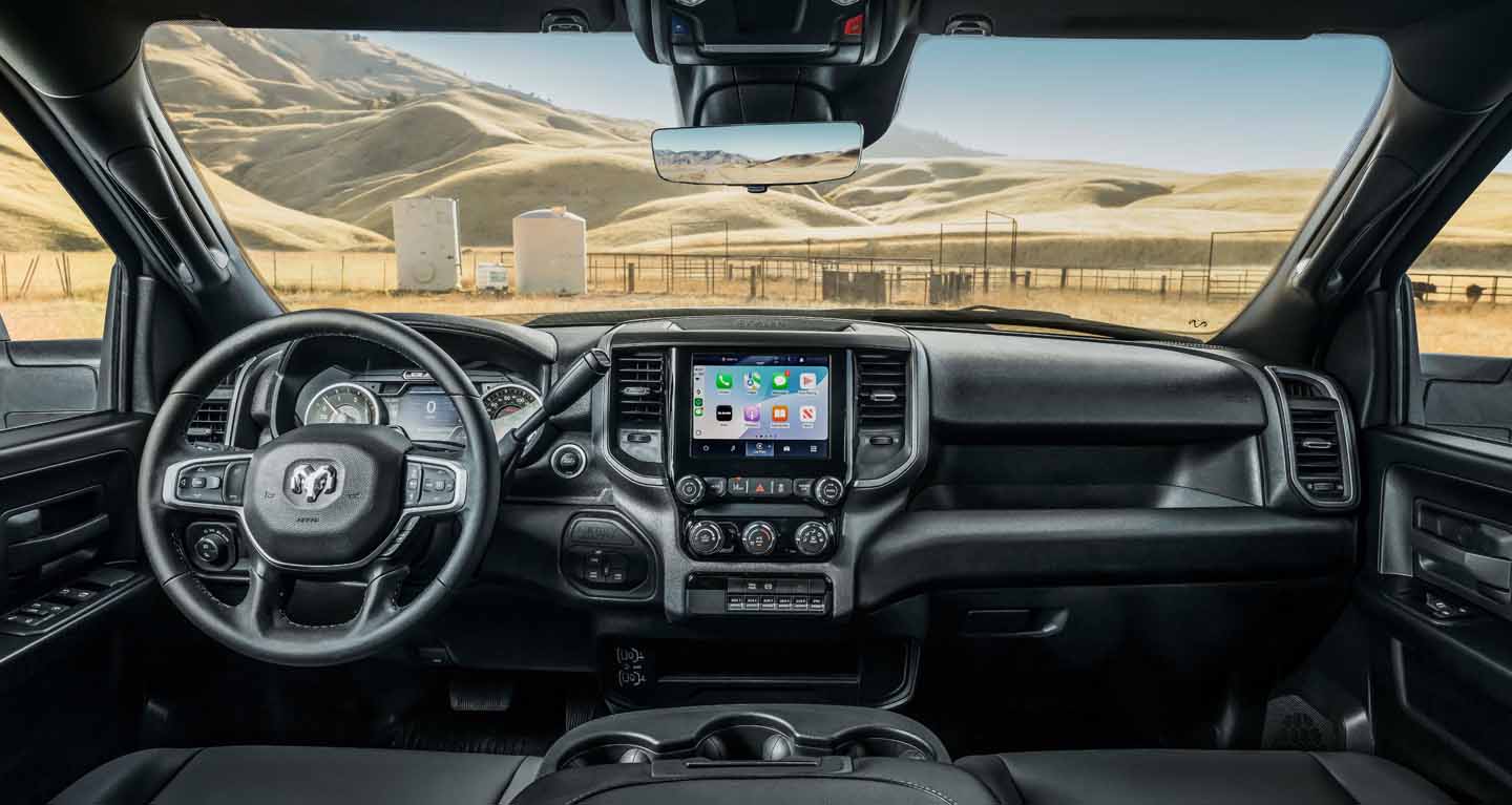 Se muestra el área de asientos delanteros de una Ram Tradesman Chassis Cab 2026 donde se destacan el volante, la pantalla digital situada en el panel de instrumentos, la pantalla táctil de Uconnect y los controles de la consola central.