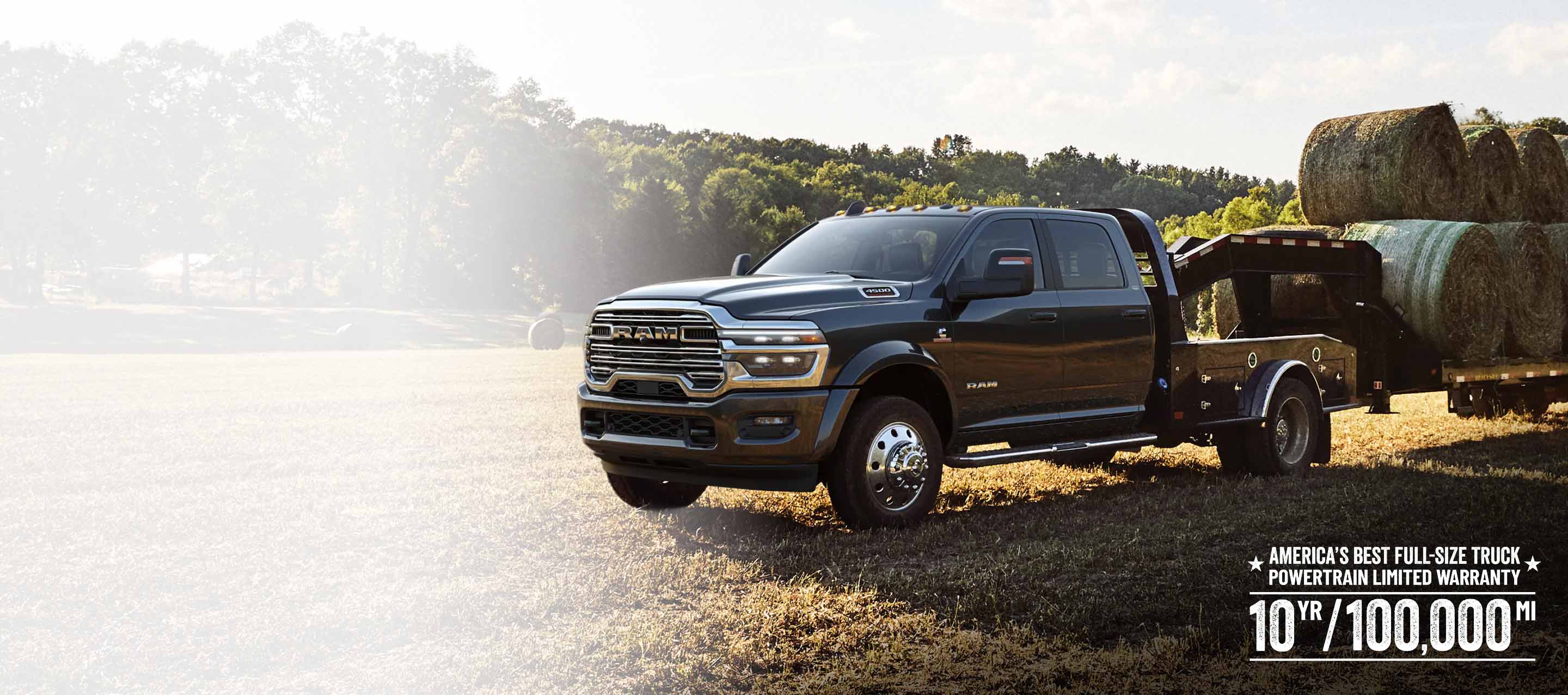 A black 2026 Ram 4500 Big Horn Chassis Cab Crew Cab with the Laramie Trim Group and a gooseneck trailer loaded with several large bales of hay, parked in an open field. America's Best Full-Size Truck Powertrain Limited Warranty. 10 Year/100,000 Mile.