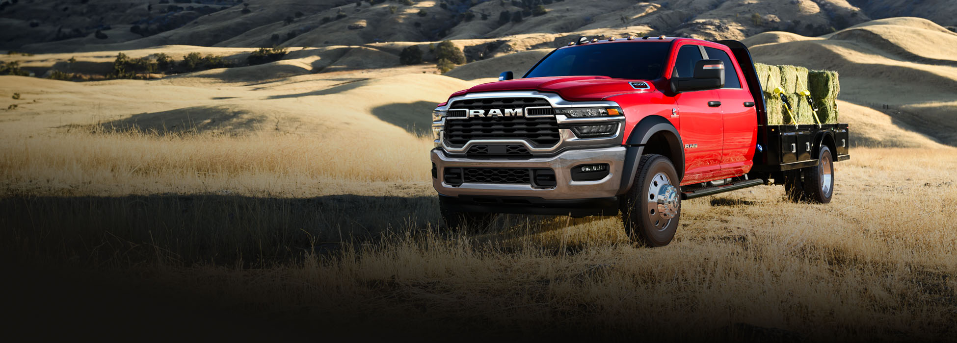 Una Ram 4500 Big Horn 4x2 Chassis Cab Crew Cab 2026 roja, con varios fardos de heno en su caja tipo plataforma, avanza por un campo.