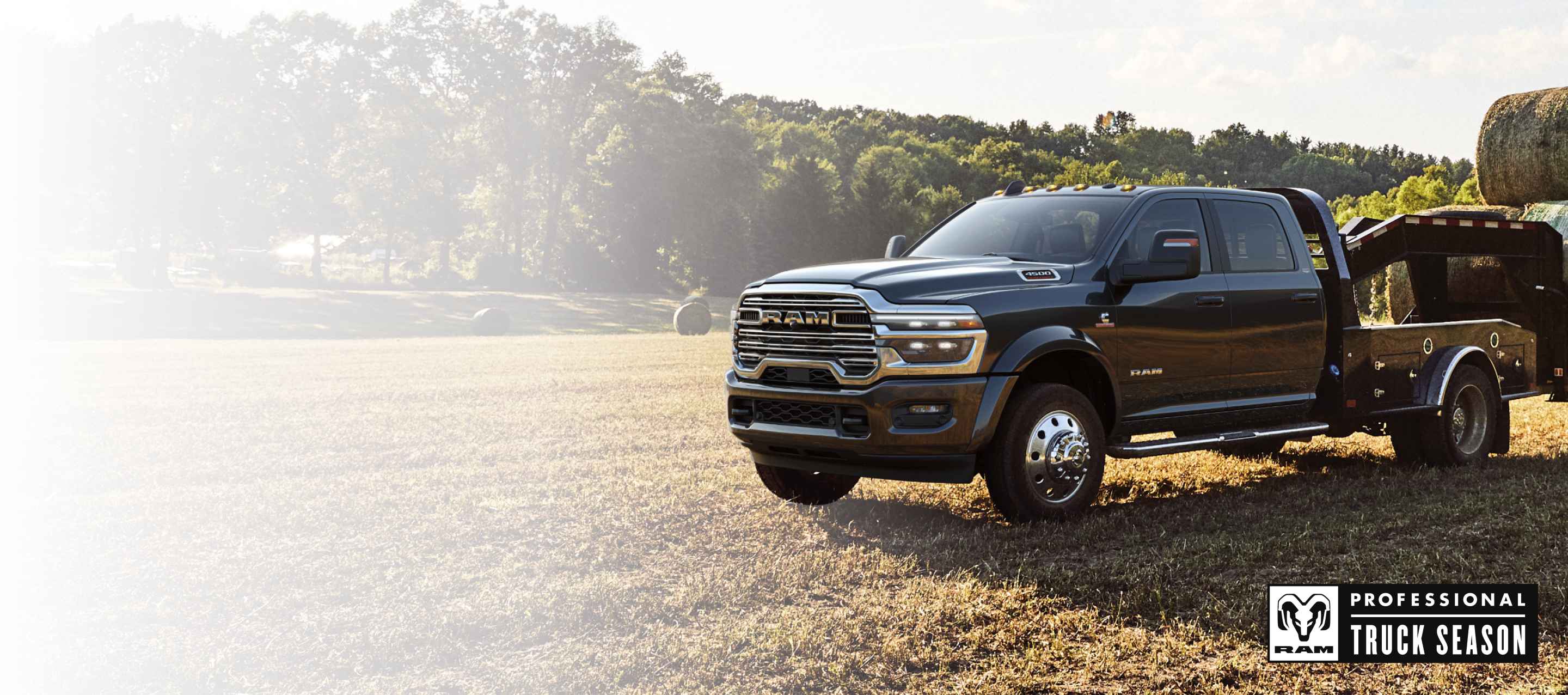 Una Ram 5500 Laramie Chassis Cab Crew Cab 2026 negra con un remolque tipo cuello de cisne cargado con varios fardos de heno, estacionada en un campo abierto. Temporada de camionetas Ram Professional.