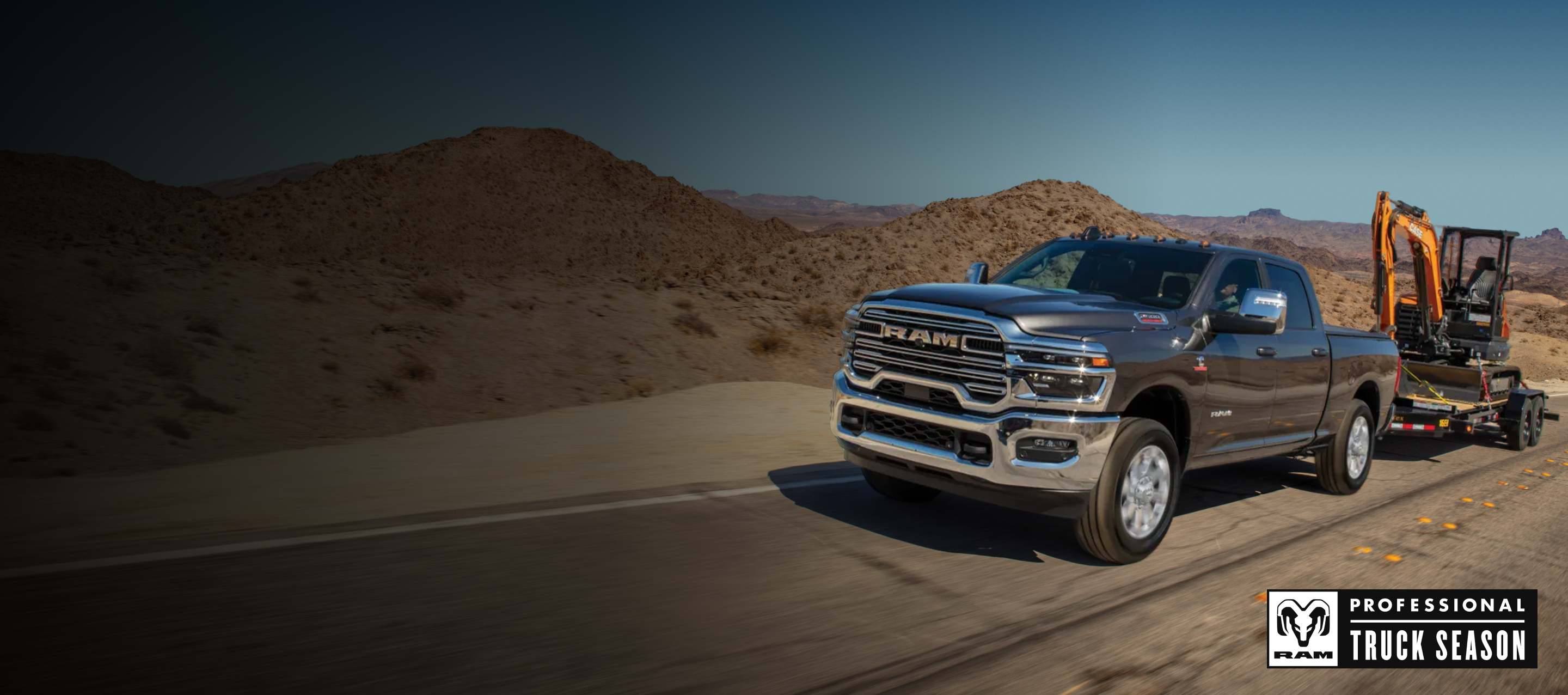 A black 2026 Ram 2500 Laramie 4x4 Crew Cab traveling down a highway, towing an excavator on a flat bed trailer. Temporada de camionetas Ram Professional.
