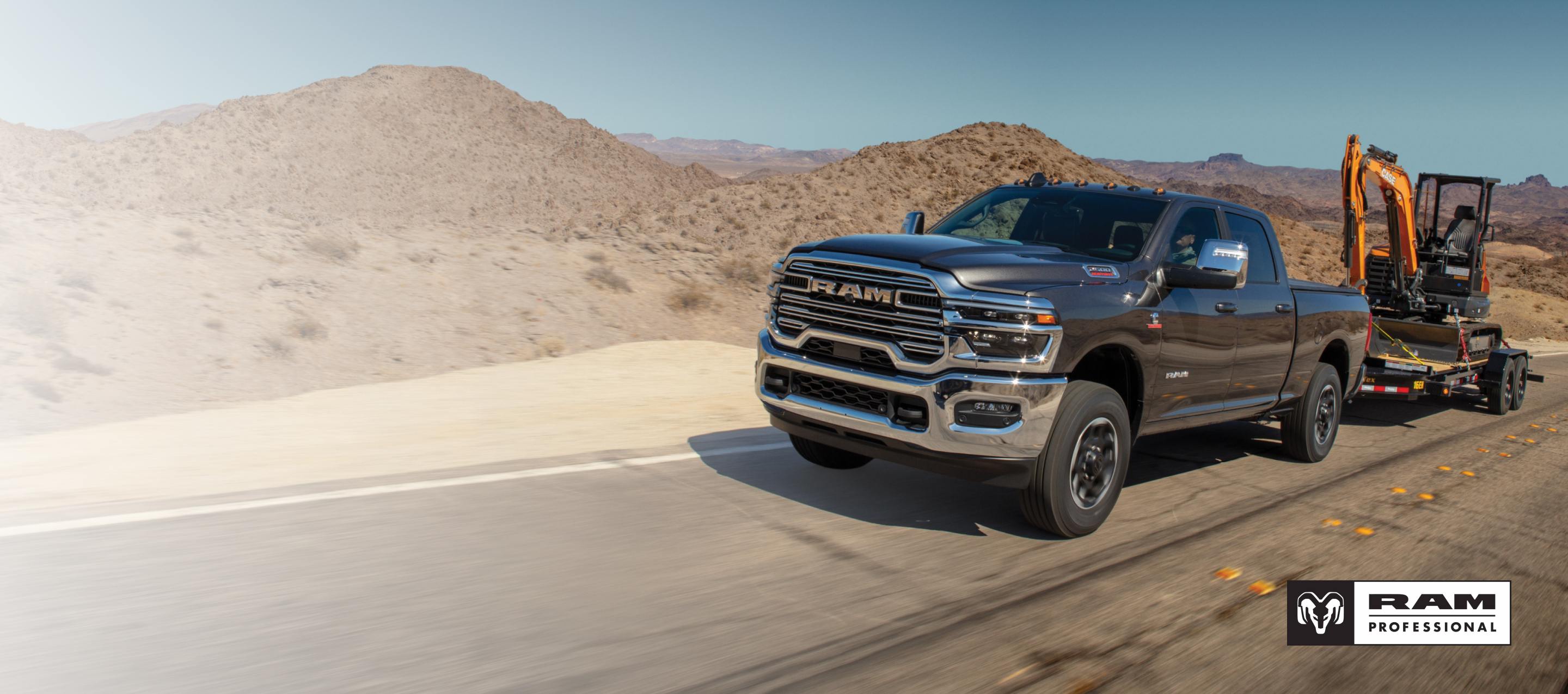 Una Ram 2500 Laramie 4x4 Crew Cab 2026 negra circulando por una autopista y remolcando una excavadora sobre un remolque de plataforma plana. Ram Professional.