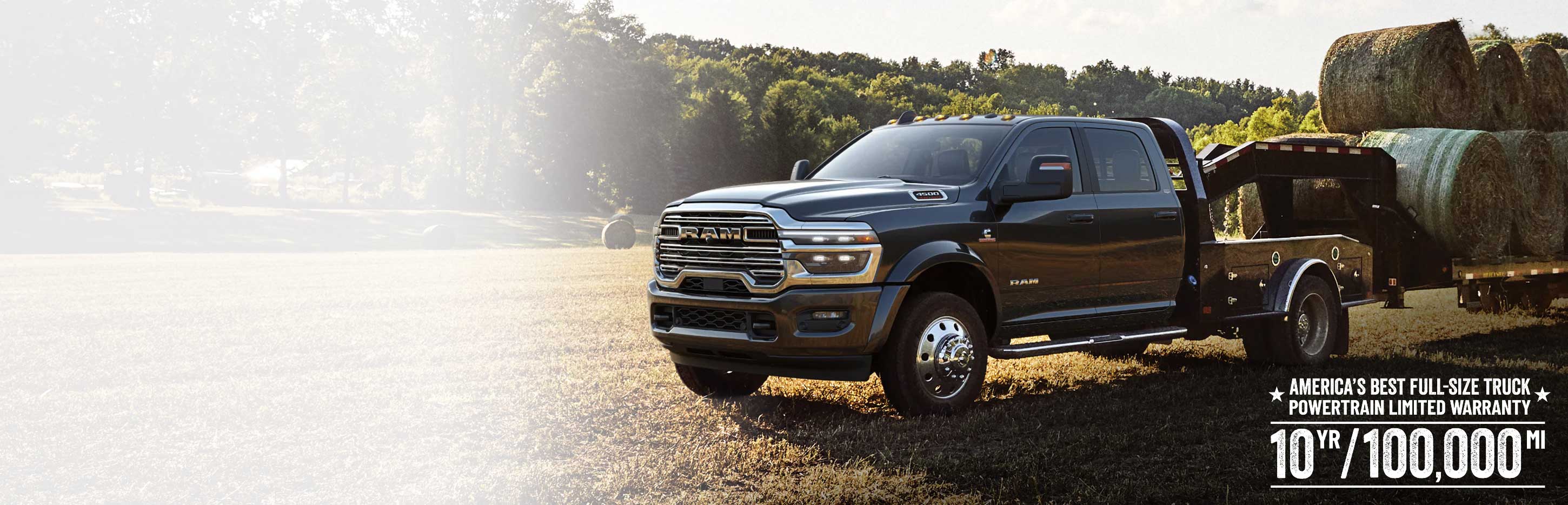 Una camioneta Ram 4500 Big Horn Chassis Cab Crew Cab 2026 negra con el paquete de equipamiento Laramie y un remolque de cuello de cisne cargado con varios fardos de heno grandes, estacionada en un campo abierto. La mejor garantía limitada para trenes motrices de camionetas de tamaño completo de los Estados Unidos: 10 años/100,000 millas.