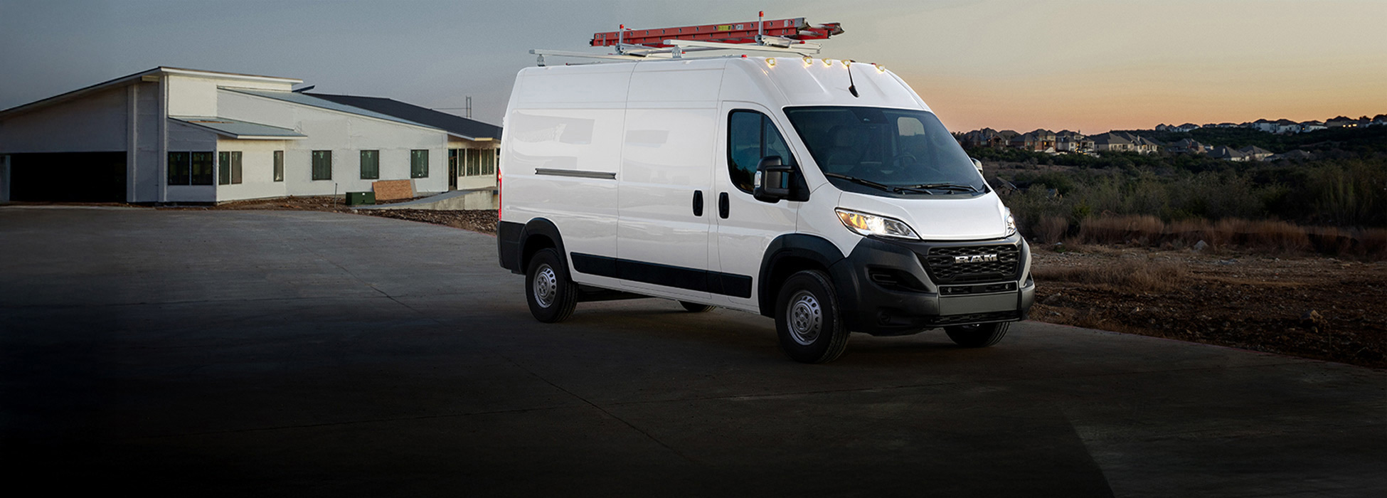 Ángulo frontal del lado del pasajero de una Ram ProMaster Tradesman Cargo Van High Roof 2026 blanca y una escalera en la parrilla del techo saliendo de una obra en construcción.