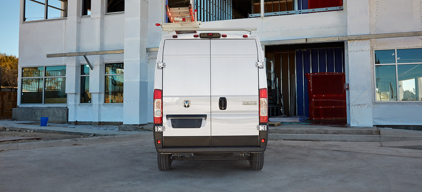 Se muestra la parte trasera de una Ram ProMaster 2500 Cargo Van High Roof 2026 blanca con un soporte para escalera, ingresando en el garaje de un edificio comercial.