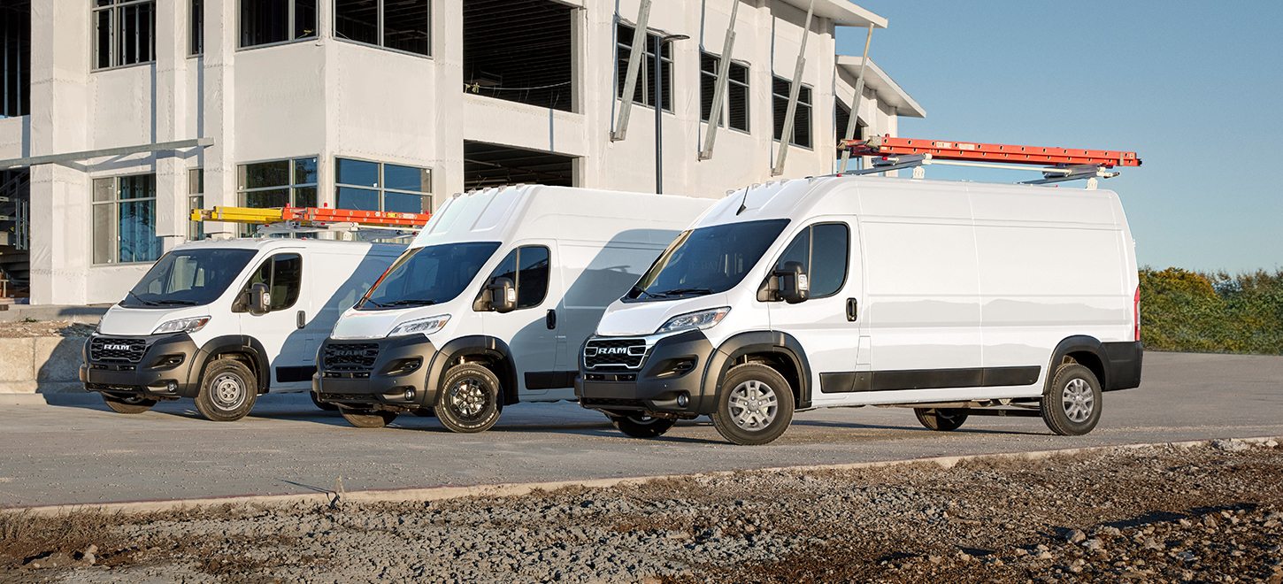 Se muestra una gama de tres vans Ram ProMaster 2026 blancas estacionadas en una obra en construcción. De izquierda a derecha: una Ram ProMaster 1500 Tradesman Cargo Van Standard Roof, una Ram ProMaster 3500 SLT Plus Cargo Van Super High Roof con el paquete de apariencia negro y una Ram ProMaster 2500 SLT Cargo Van High Roof.