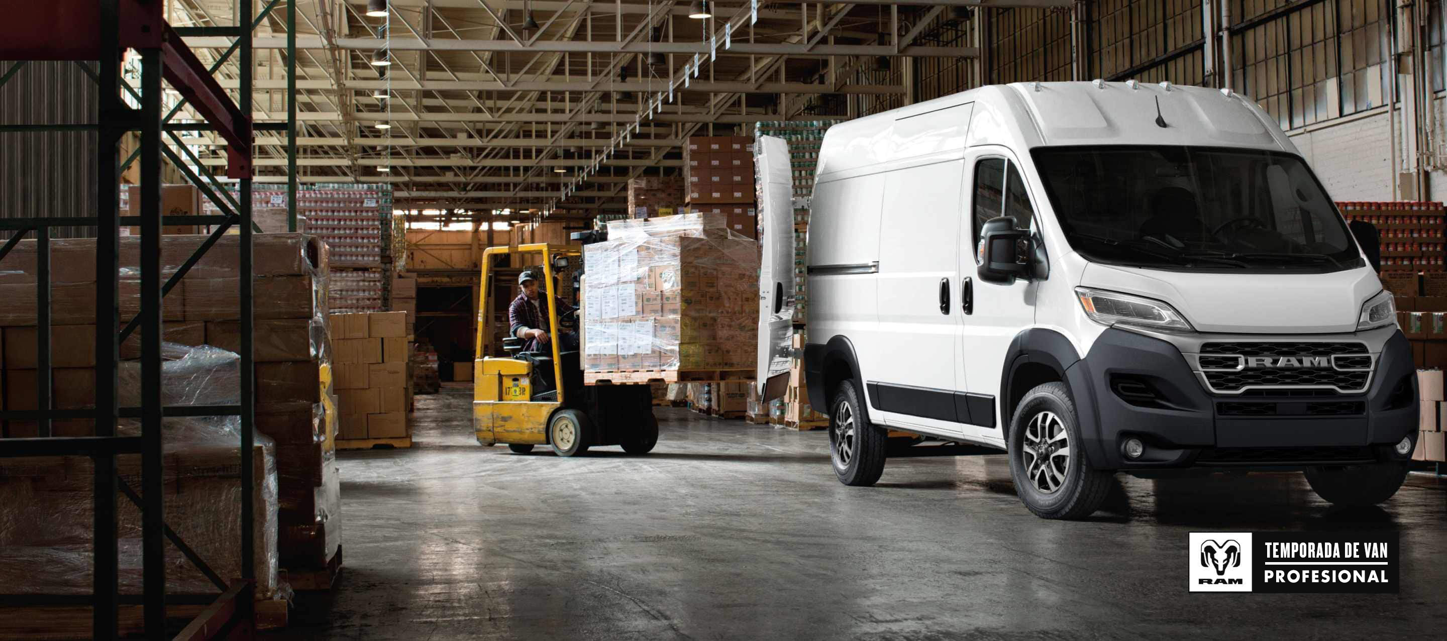 Un ángulo delantero del lado del pasajero de una Ram ProMaster 2500 SLT Cargo Van High Roof 2026 blanca estacionada en un depósito con las puertas traseras totalmente abiertas y un montacargas con una pila de cajas circulando hacia la parte trasera de la van. Temporada de vans profesionales Ram.