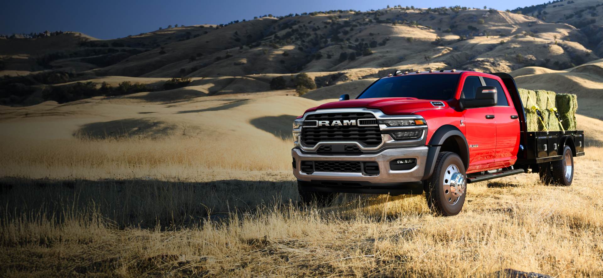Una Ram 4500 Big Horn 4x2 Chassis Cab Crew Cab 2026 roja trasladando varios fardos de heno grandes en una mejora de plataforma larga.