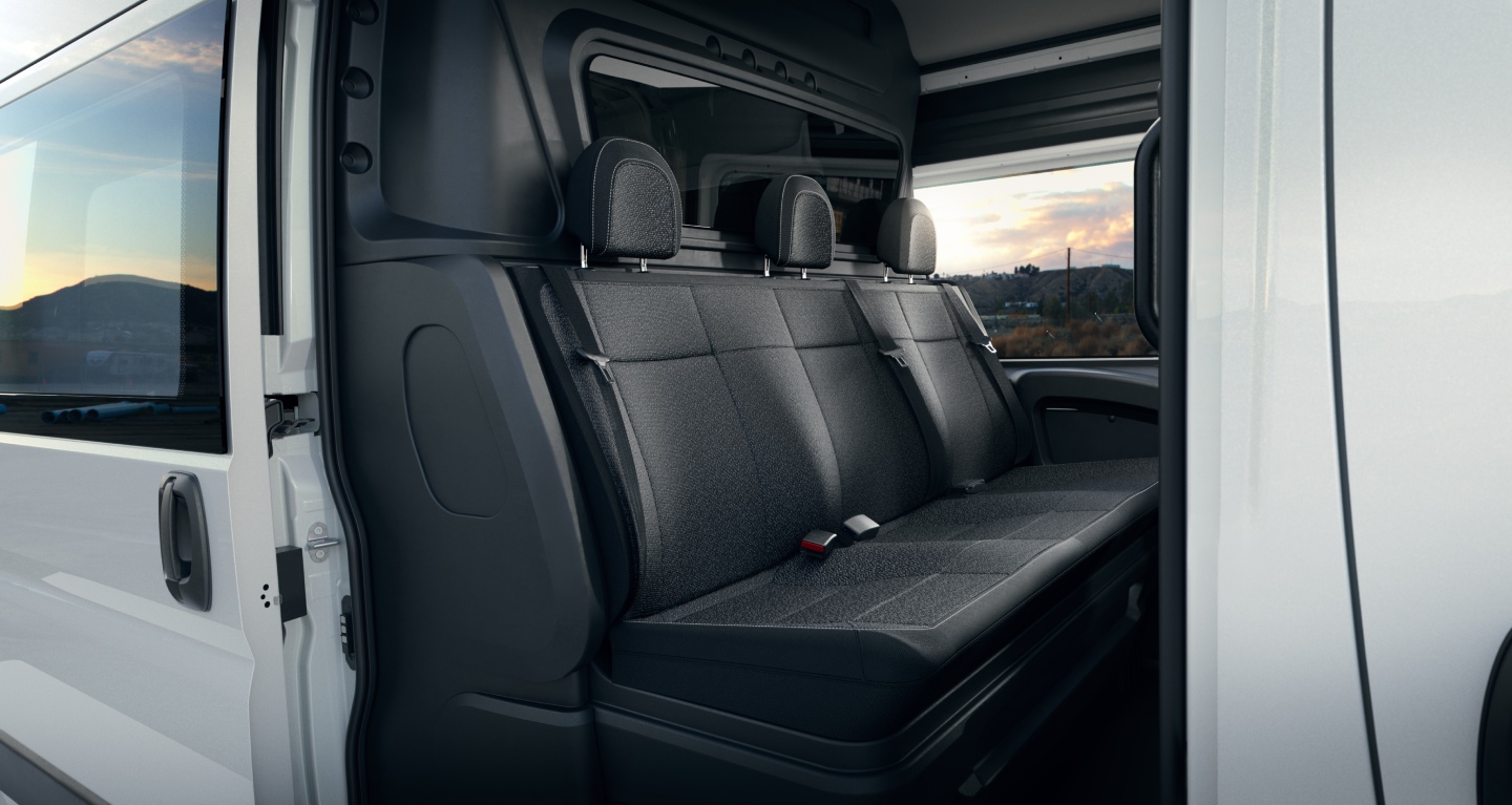 Display The rear seats in a white 2027 Ram ProMaster 2500 Tradesman High Roof Cargo Van with the Crew Van Package, shot through the open passenger-side sliding door.