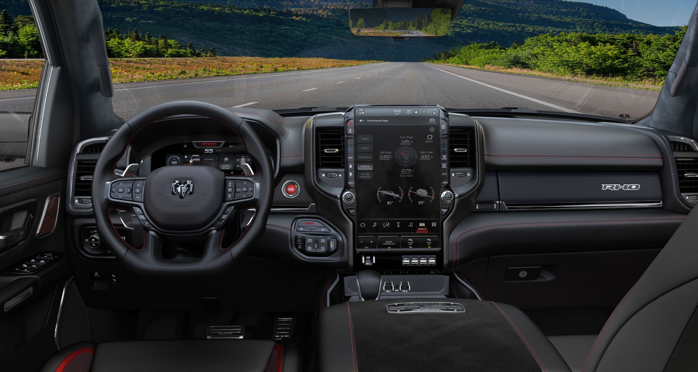 Muestra El interior de la Ram 1500 RHO 4x4 Crew Cab 2027, con especial atención al volante, la pantalla digital del tablero, la pantalla táctil Uconnect y los controles de la consola central.
