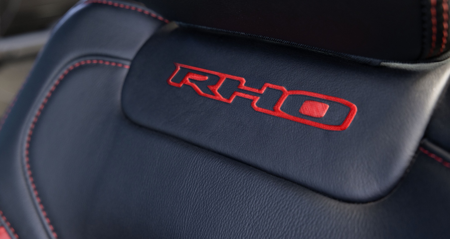 Muestra Letras RHO bordadas en hilo rojo justo debajo del apoyacabezas del asiento del conductor de la Ram 1500 RHO 4x4 Crew Cab 2027.