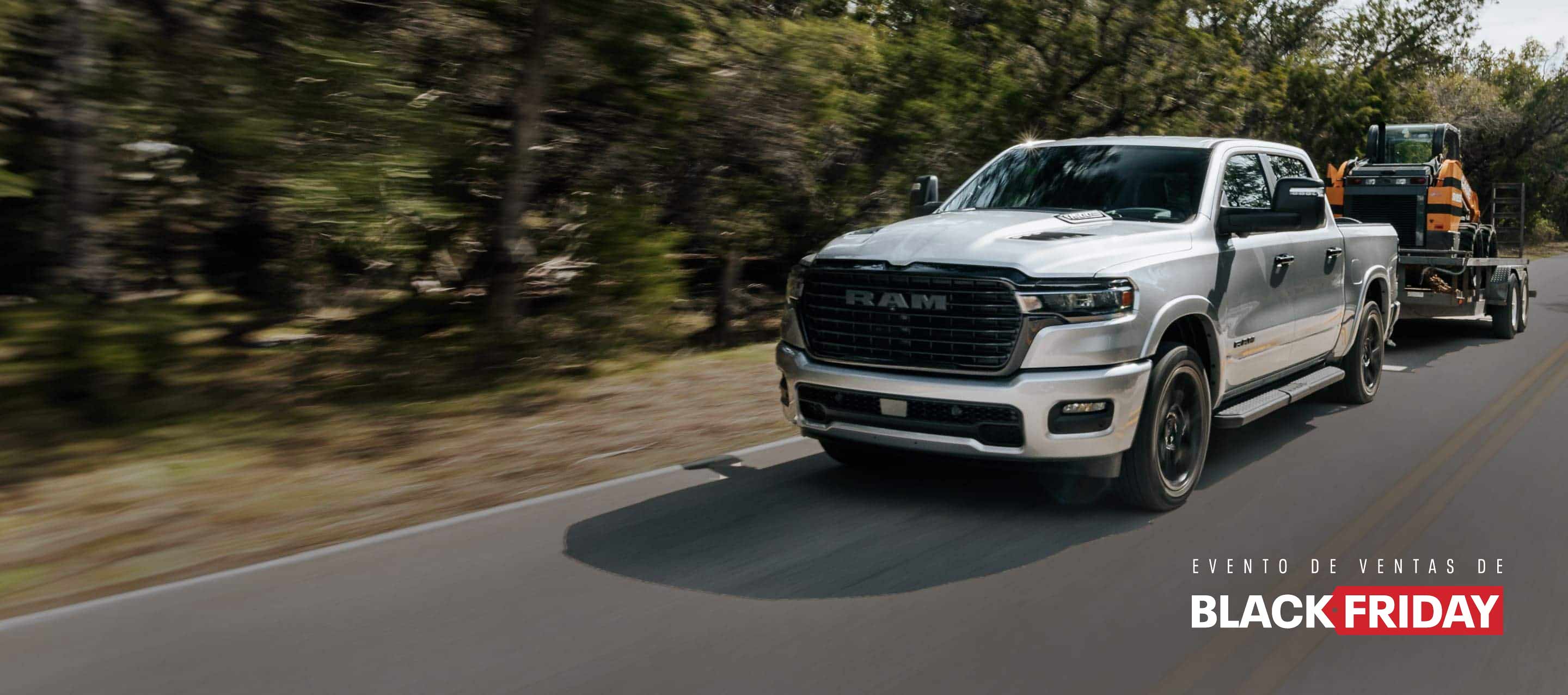 Una Ram 1500 Laramie 4x4 Crew Cab 2025 plateada circulando por una carretera rural, acarreando equipo para movimiento de tierras en un remolque basculante. Evento del Black Friday.