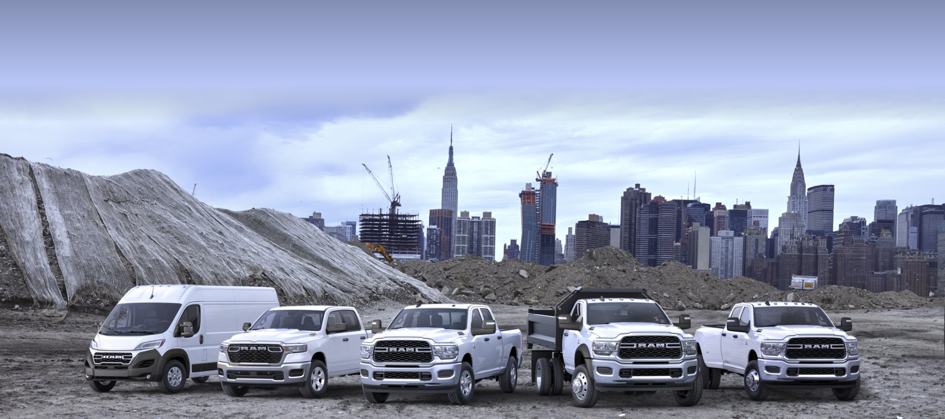 La línea de la marca Ram en blanco, en una obra de construcción. De izquierda a derecha: una Ram ProMaster 3500 SLT High Roof Cargo Van 2024, una Ram 1500 Tradesman 4x4 Crew Cab 2025, una Ram 2500 Tradesman 4x4 Crew Cab 2024, una Ram 5500 Tradesman Chassis Regular Cab 2024 con una mejora de carrocería volcadora y una Ram 3500 Tradesman 4x4 Crew Cab 2024.