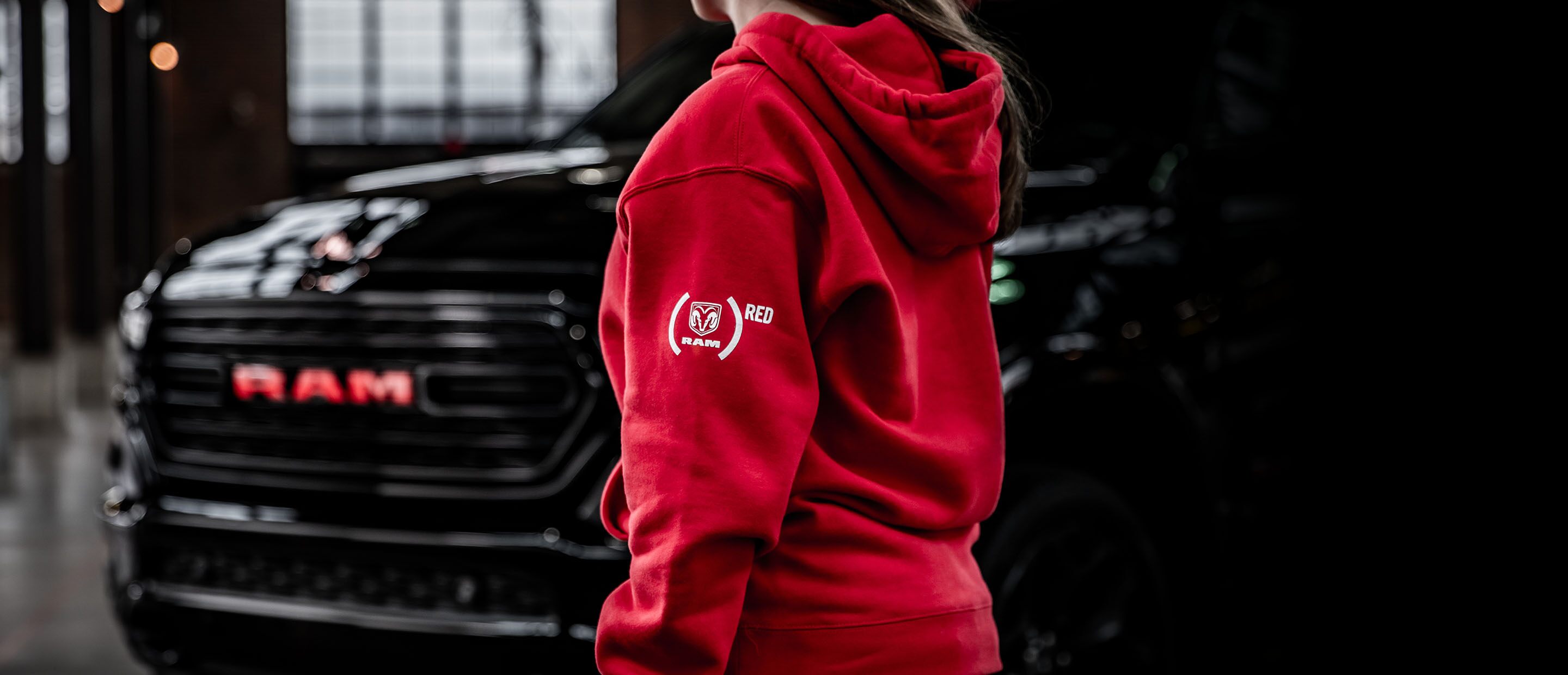 Una mujer que viste una chaqueta con capucha roja con el logo de Ram Red caminando hacia una Ram 1500 Limited Ram Red Edition 2023.