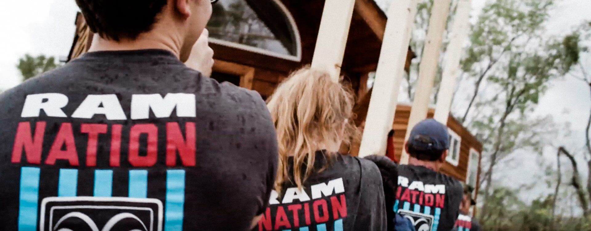 Grupo de voluntarios que viste camisetas de Ram Nation y transportan leña hacia una casa.