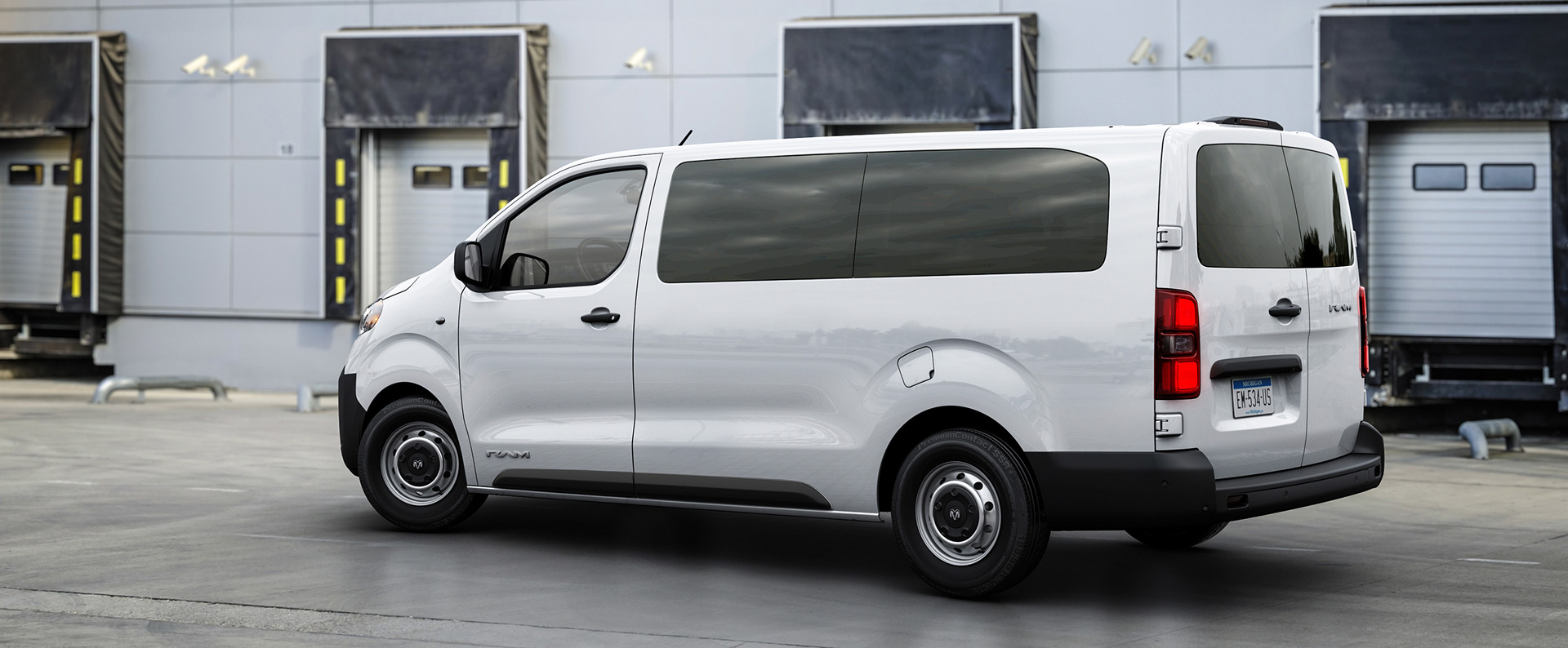 Vista trasera de medio perfil del lado del conductor de una Ram ProMaster City® Tradesman Cargo Van 2027 en White con vidrios laterales y traseros polarizados, puertas traseras dobles cerradas, estacionada junto a un muelle de carga.