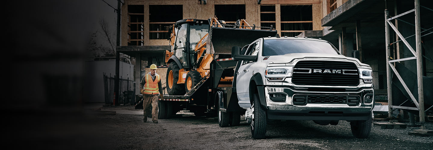 Ram Chassis Cab con plataforma remolcando otro vehículo en un sitio de construcción.