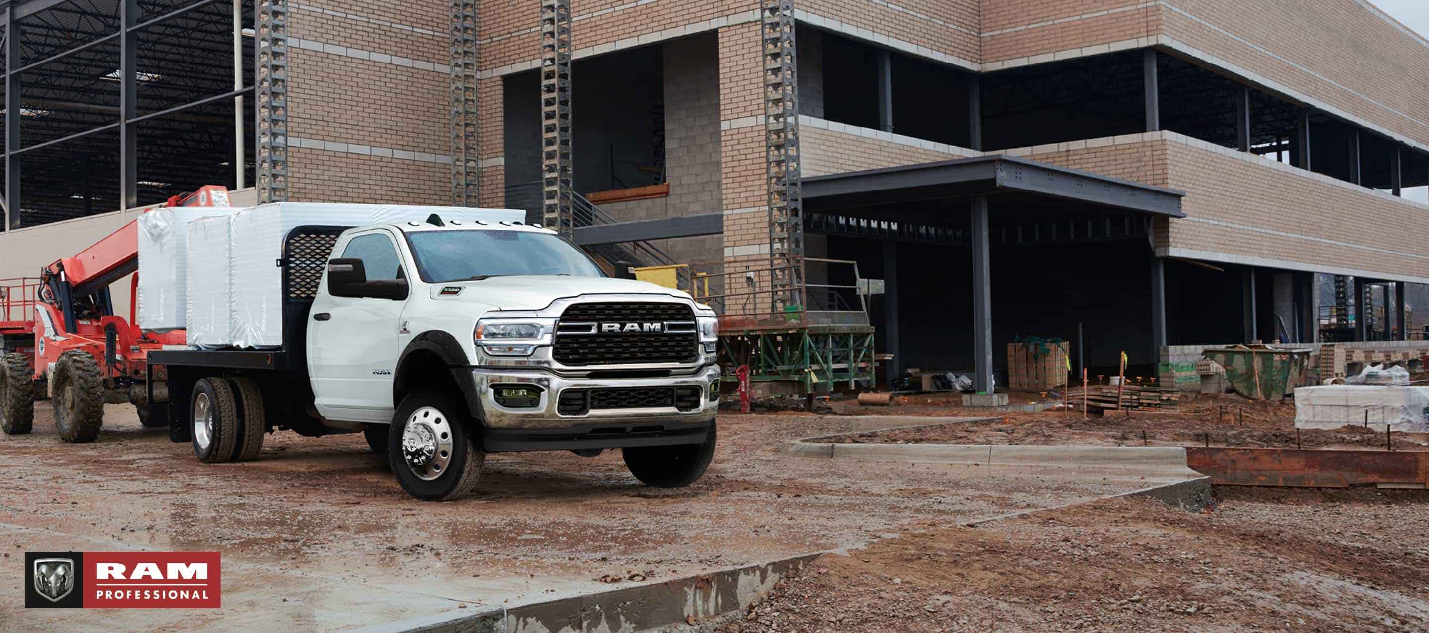 Una Ram Chassis Cab 2024 blanca con una mejora de plataforma cargada con materiales de construcción, estacionada en una obra de construcción comercial. Ram Professional.