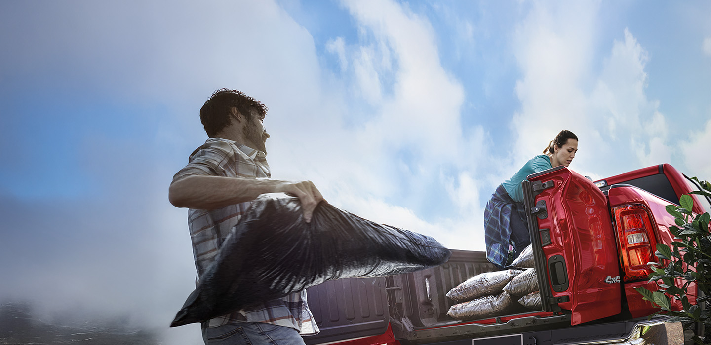 Dos personas cargando bolsas de mantillo en la plataforma de una camioneta Ram.