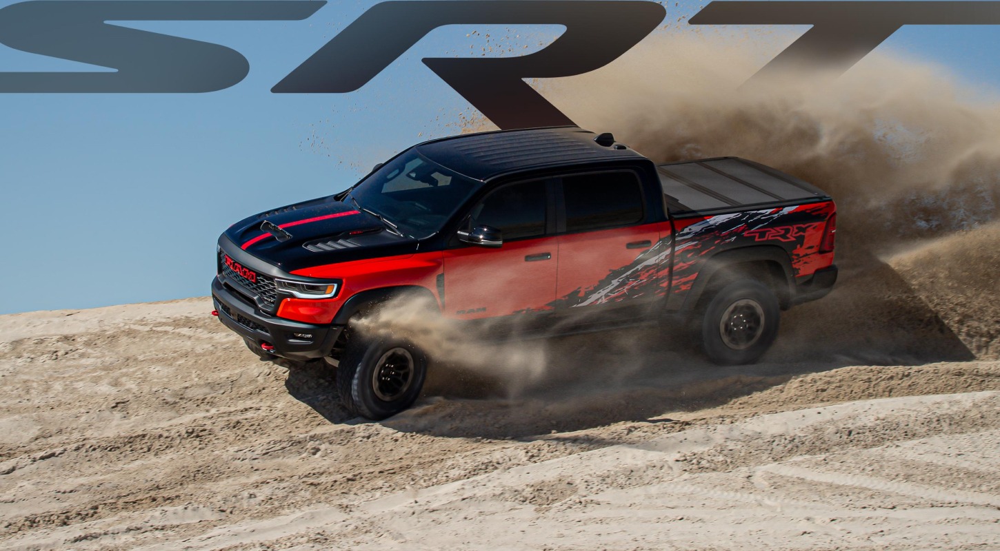 Una Ram 1500 TRX SRT Bloodshot Night Edition 4x4 Crew Cab 2027 roja, con el capó y el techo negros y gráficos especiales de salpicaduras en los laterales de la plataforma, levantando arena mientras recorre el desierto. SRT.