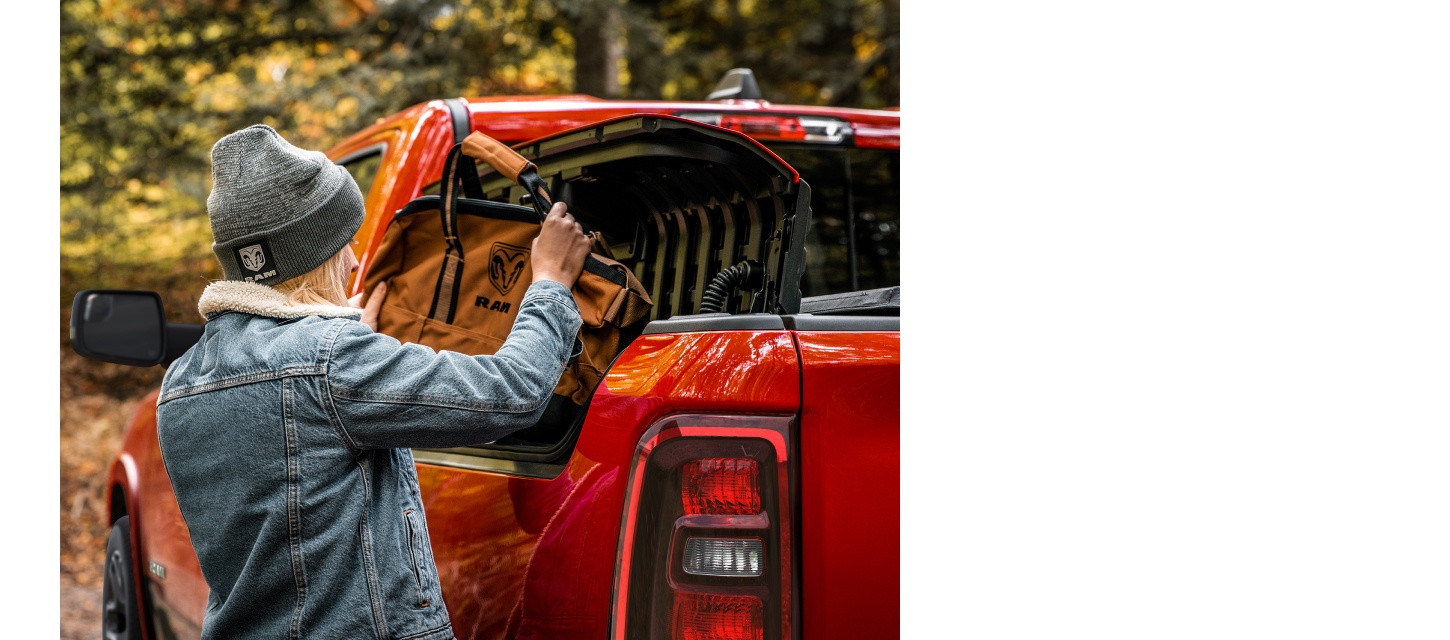 Una persona sacando un bolso de lona marca Ram de la Ram Box de una Ram 1500 Laramie 4x4 Crew Cab roja.