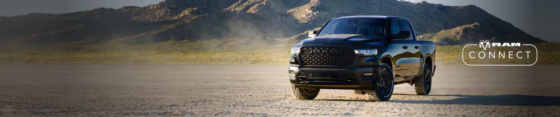 A driver-side front angle of a black 2026 Ram 1500 Warlock Crew Cab parked on a clearing with mountains in the background. The Ram Connect logo.