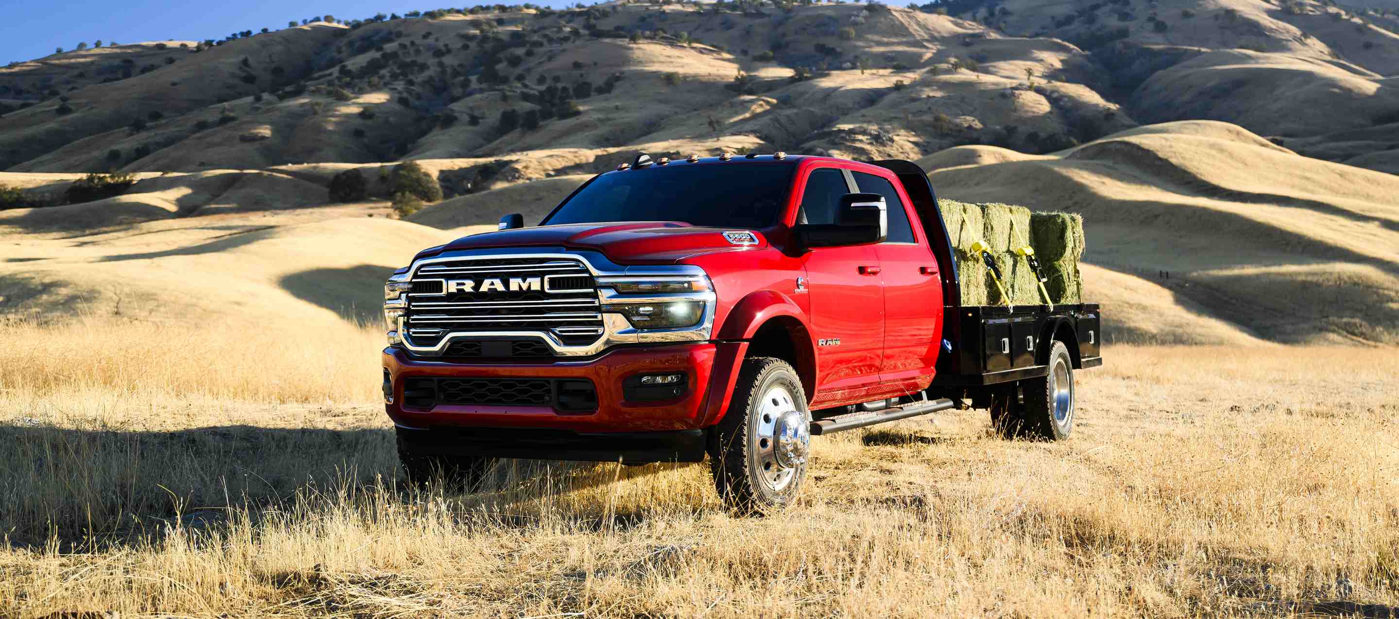 Una Ram 5500 Laramie Chassis Cab Crew Cab 2025 roja trasladando varios fardos de heno grandes en una mejora de plataforma larga.